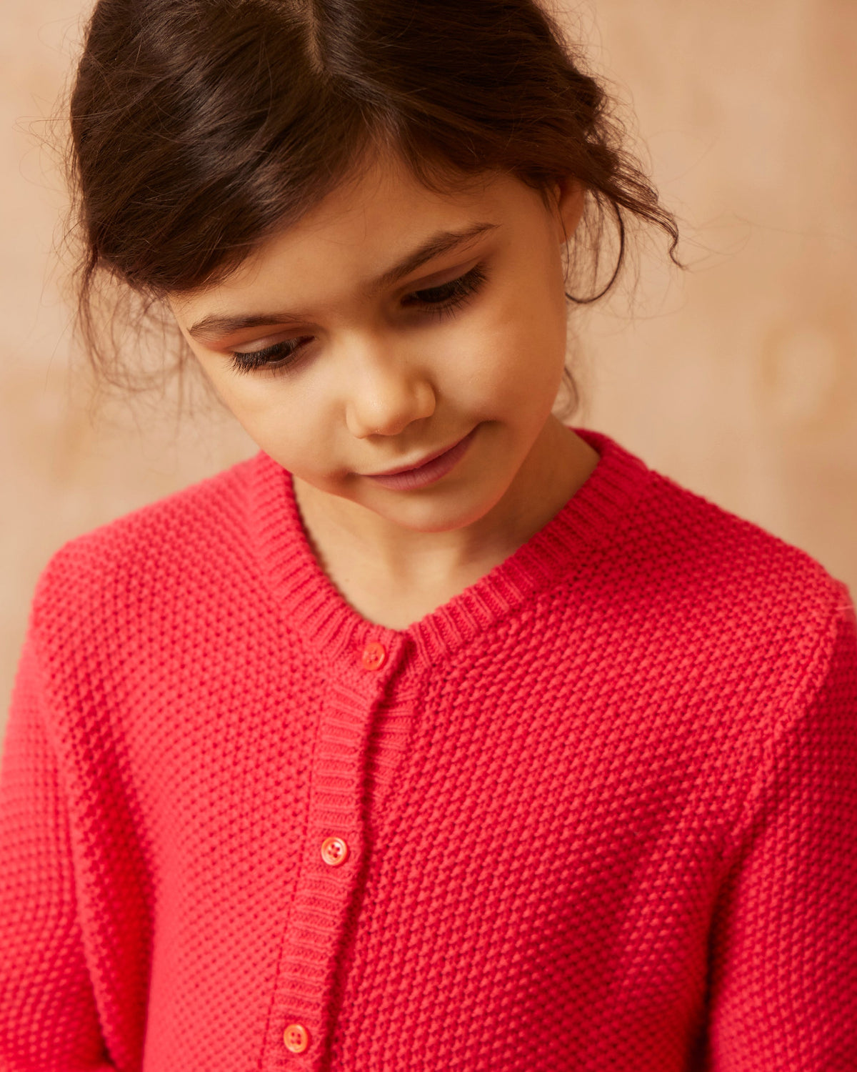Close-up of the button-front and ruffle hem on the raspberry Moss Stitch Cardigan from MIKA & MILO