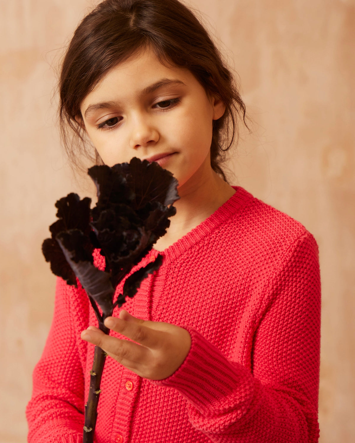 Girl wearing the raspberry Moss Stitch Cardigan from MIKA & MILO in soft natural light