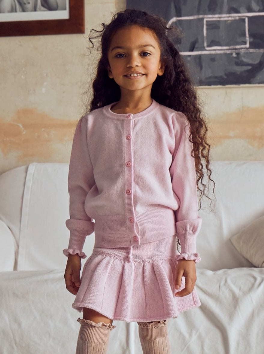 This stylish 2 ply cardigan comes with gentle puff sleeves, a long bottom rib to accentuate the waist, and sweet ruffles at the end of the cuff. A fun light weight addition to any winter wardrobe, it is made with the softest cashmere/merino blend from Inner Mongolia, and will keep your Little One stylish and warm all winter long. Team it up with our matching pleated Tennis skirt in Blossom Pink or a head-to-toe cosy feel.