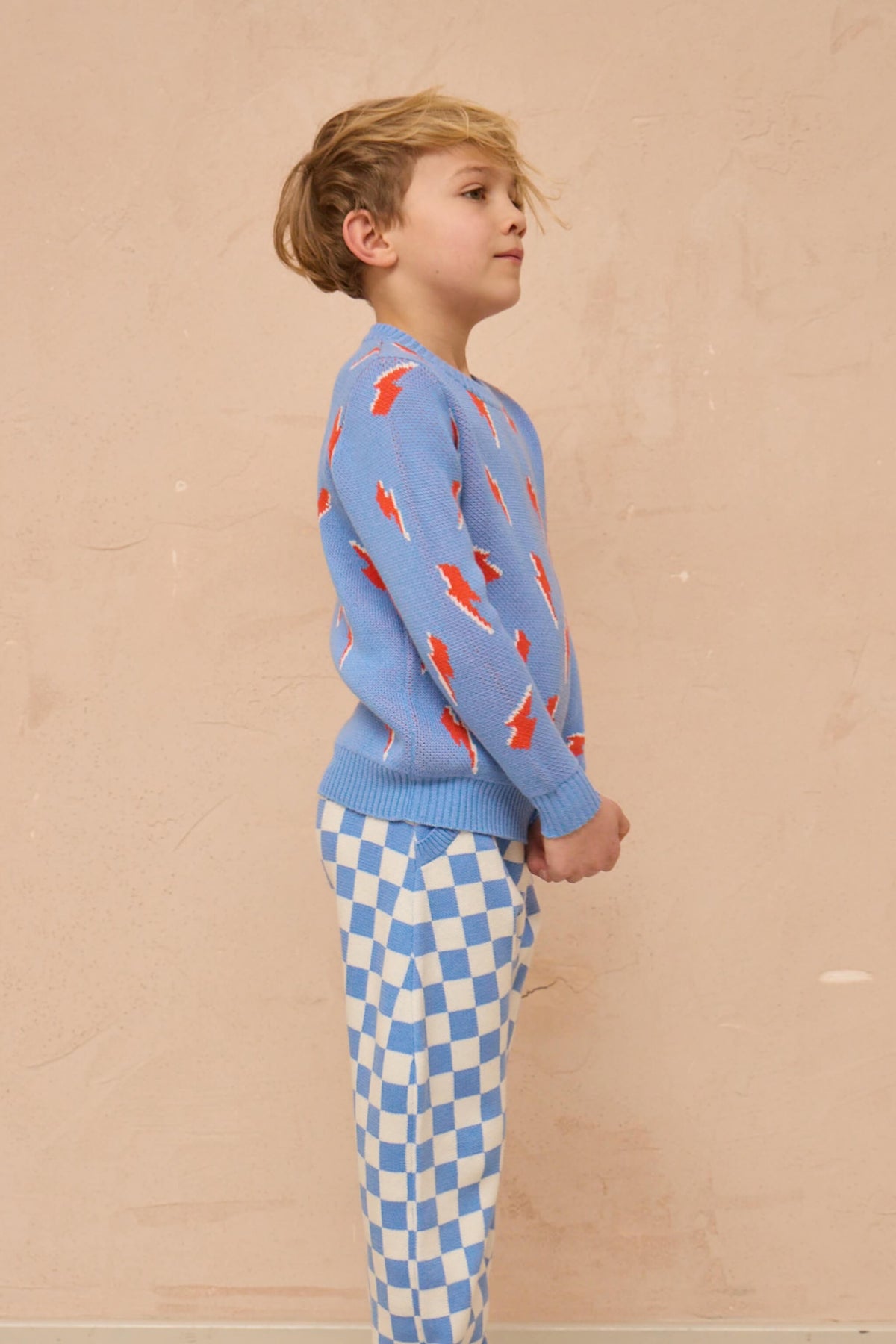 Boy standing against a plaster wall in the Bolt Storm Jumper in azure blue