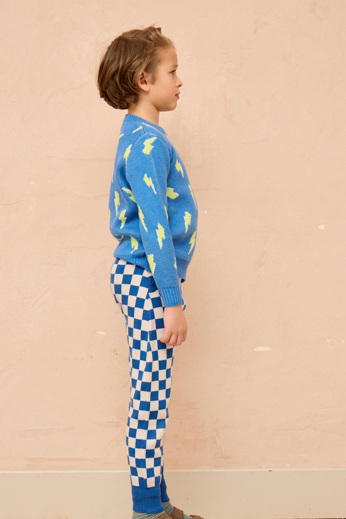 Boy standing against a plaster wall in the Bolt Storm Jumper in hussar blue