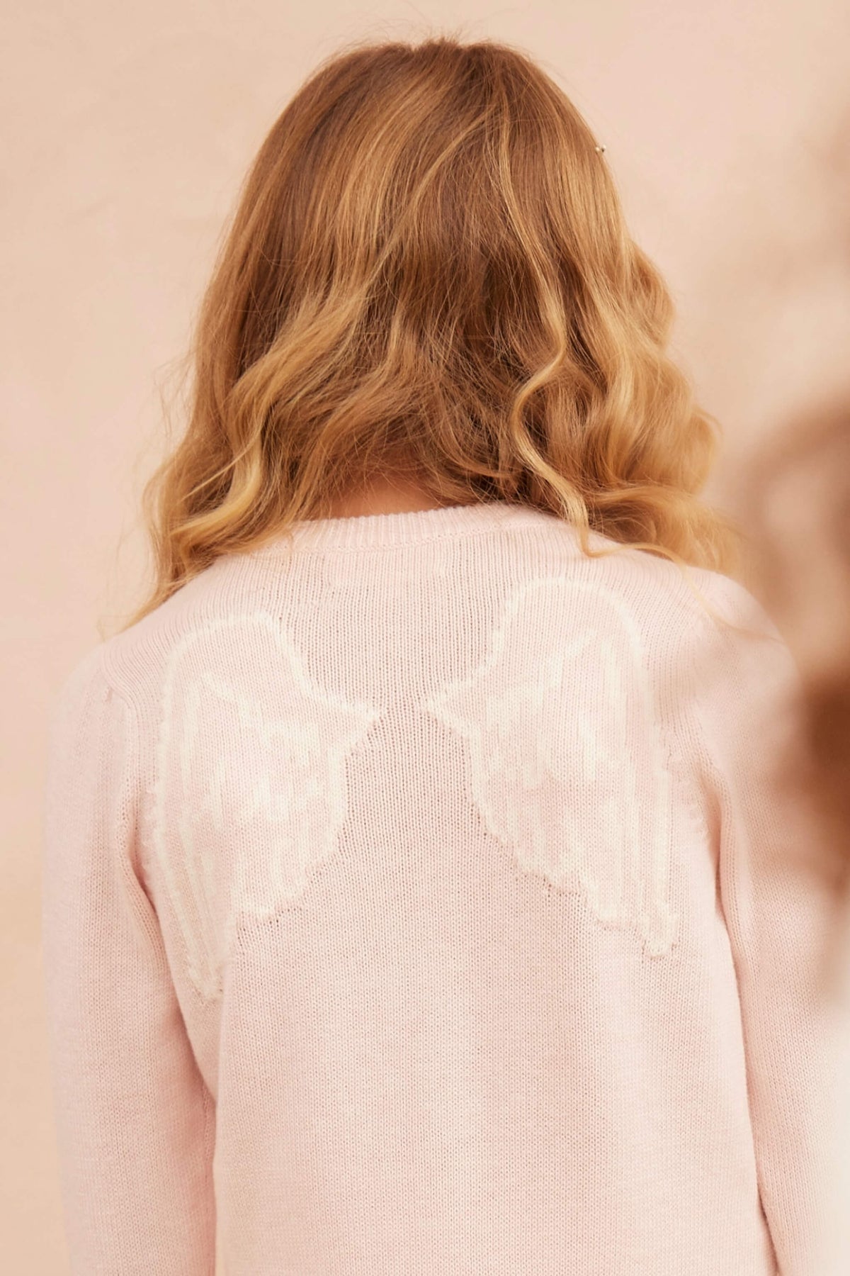 Side view of a girl in the Angel Wings Jumper in blush pink