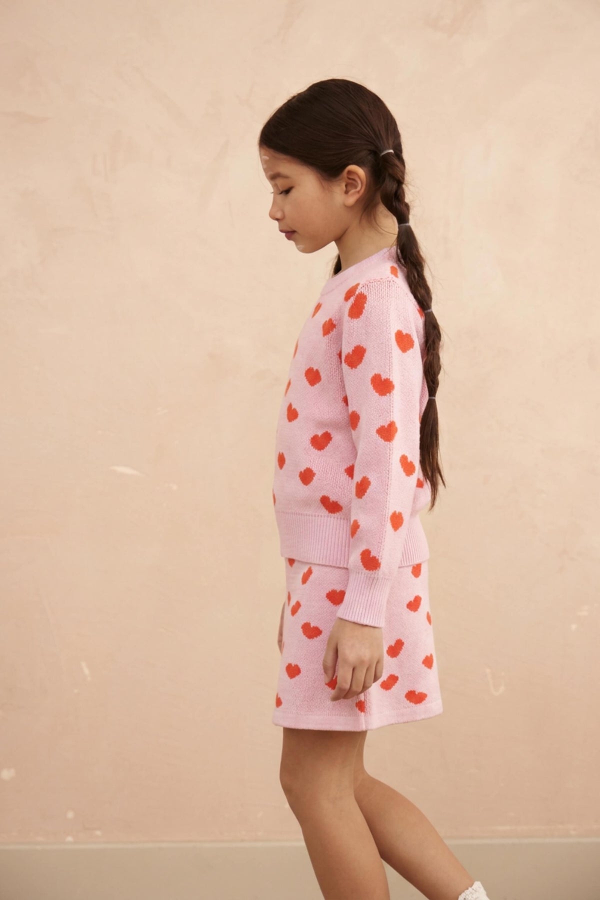 Girl standing in the Love Hearts jumper and skirt set in bubble gum pink