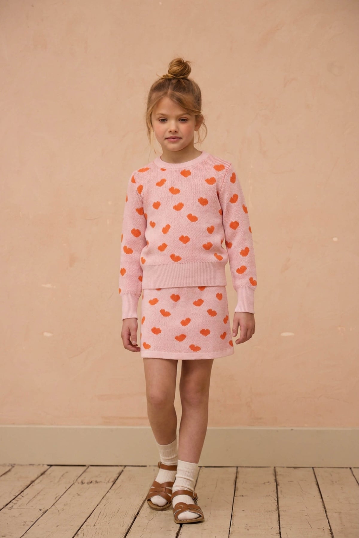 Girl wearing the Love Hearts set in rose pink against a plaster wall