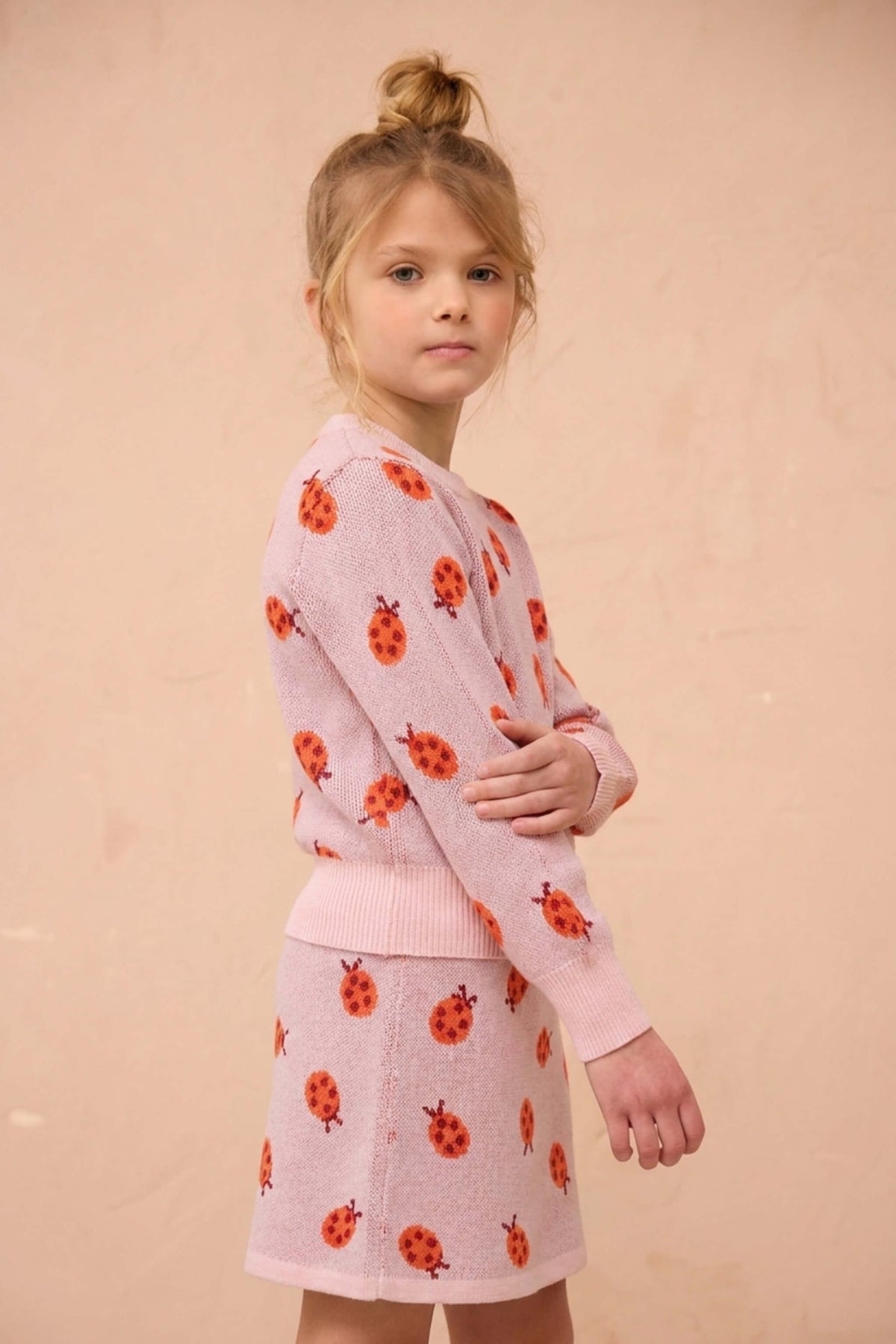 Girl standing in the Ladybird jumper and skirt set in rose pink