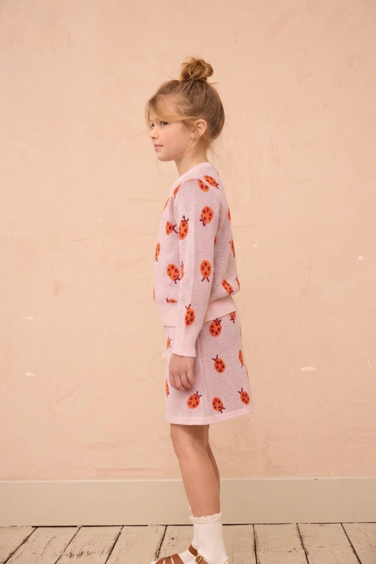 Girl standing against a plaster wall in the Ladybird set in rose pink