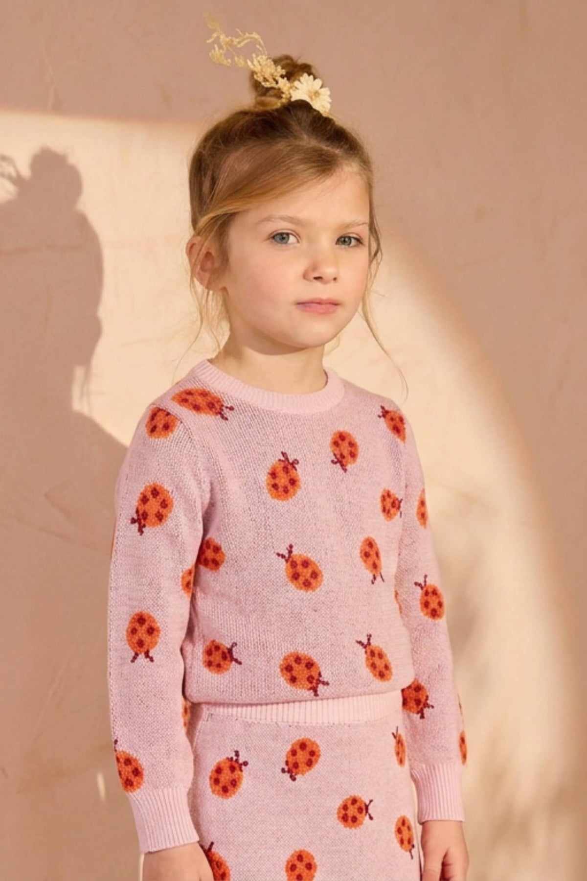 Girl wearing the Ladybird Skirt in rose pink against a plaster wall