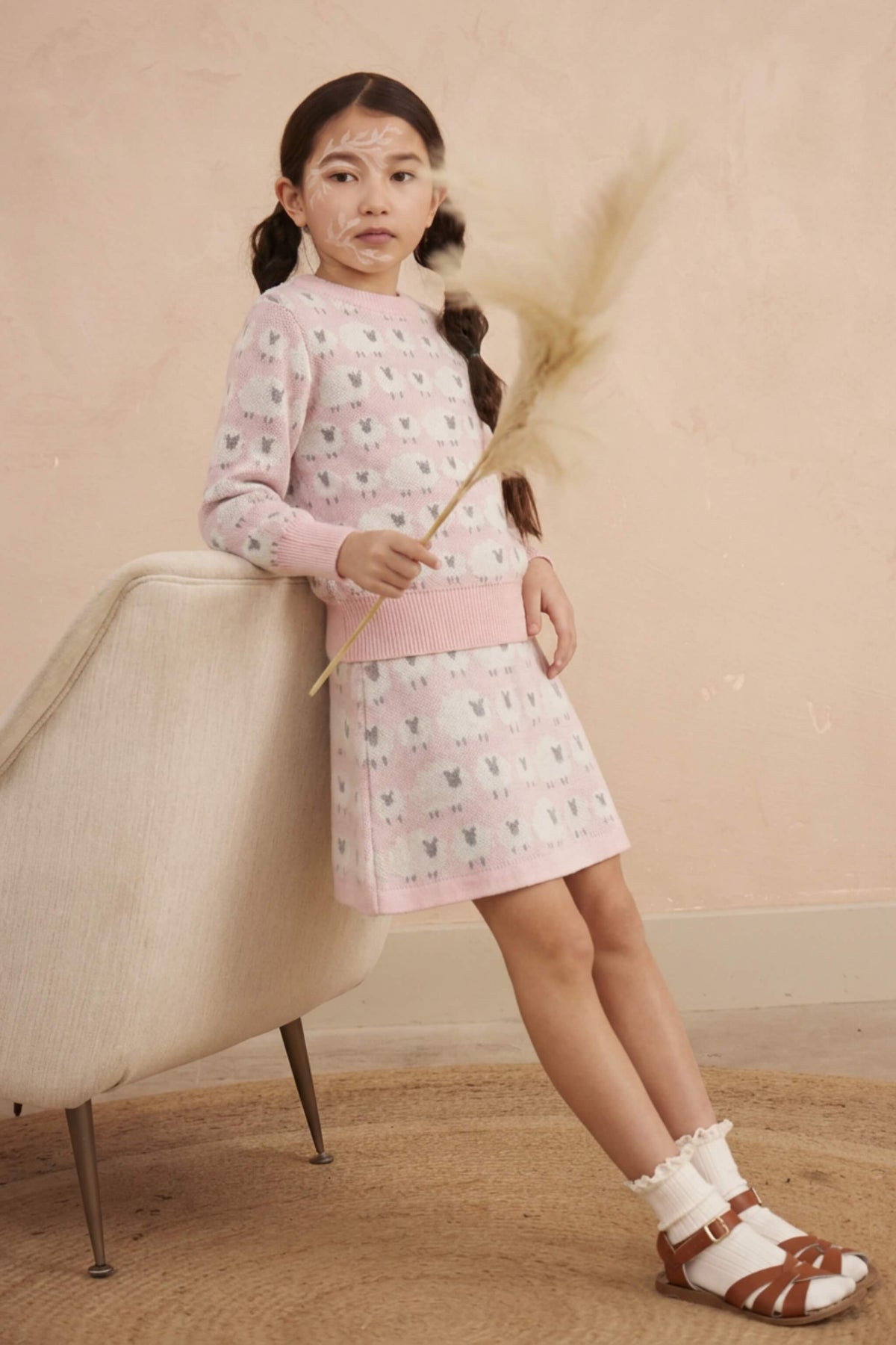Girl leaning against a chair in the Little Bo Peep jumper and skirt set in rose pink