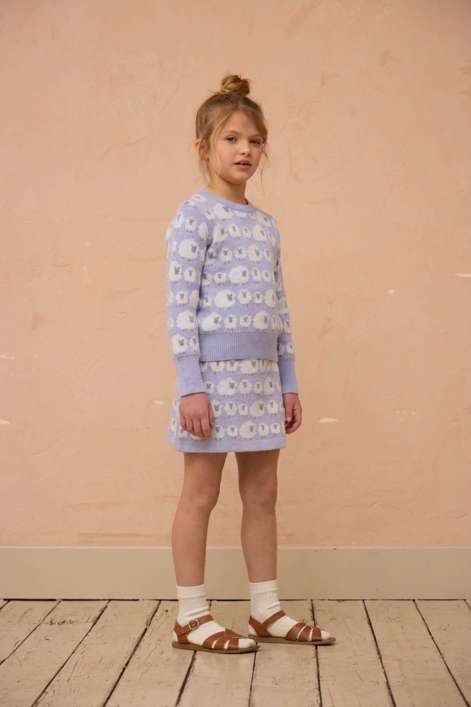 Girl standing against a plaster wall in the Little Bo Peep set in lavender