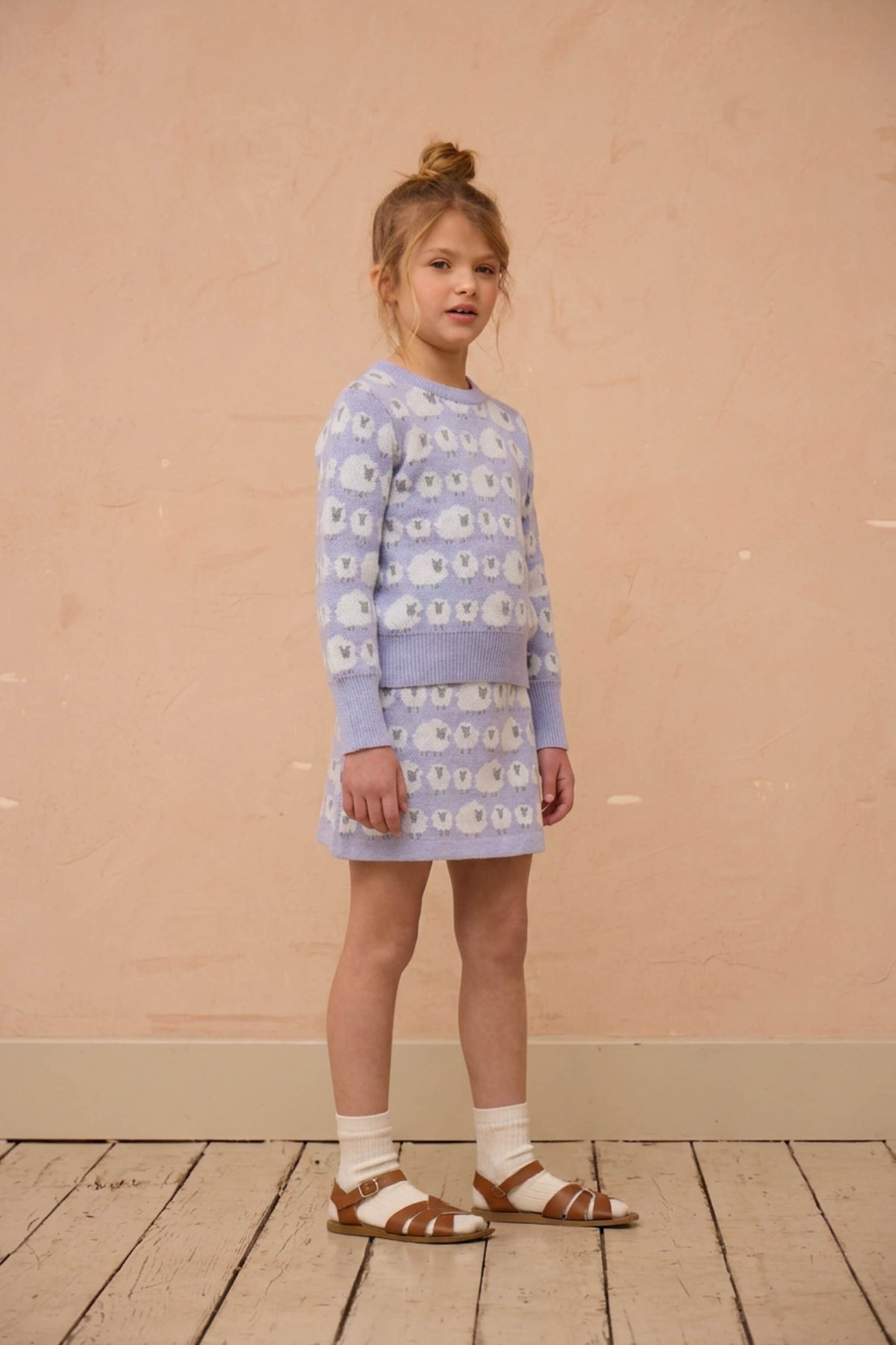 Girl standing against a plaster wall in the Little Bo Peep set in lavender